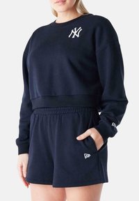 Felpa corta navy con logo sul petto e pantaloni corti abbinati. Materiale morbido, polsini a coste e vita elastica con tasche laterali.