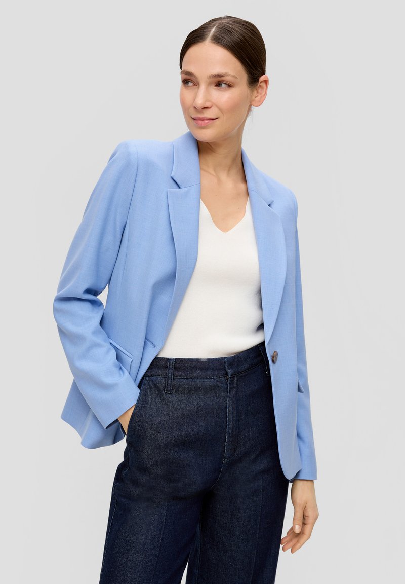 Blazer bleu clair avec une coupe ajustée, revers crantés, fermeture à un bouton, associé à un top blanc à col en V et un pantalon en denim foncé.