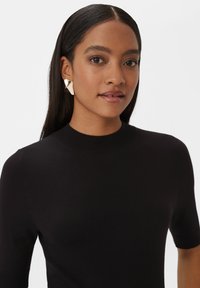 Haut en tricot noir au design cintré et aux manches courtes. D'étonnantes boucles d'oreilles en or en forme de triangle rehaussent le look contemporain. Texture lisse.