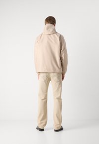 Beige jacka med huva i en mjuk textur, kombinerad med ljusbruna byxor. Outfitten har subtila sömnadsdetaljer och svarta skor.