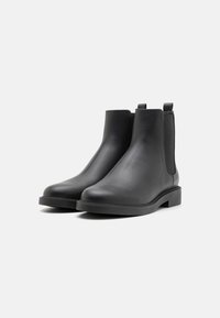 Botine Chelsea negre din piele cu panouri elastice laterale, vârf rotunjit și toc jos bloc. Textură netedă și design minimal.