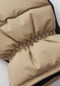 Beige padded glove with elasticated wrist, black accents, and smooth waterproof exterior. Textured surface visible, highlighting form and design.