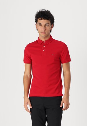 Camisa polo roja de algodón, con un cuello clásico, tapeta de tres botones, mangas cortas y un pequeño parche con el logo en el pecho.