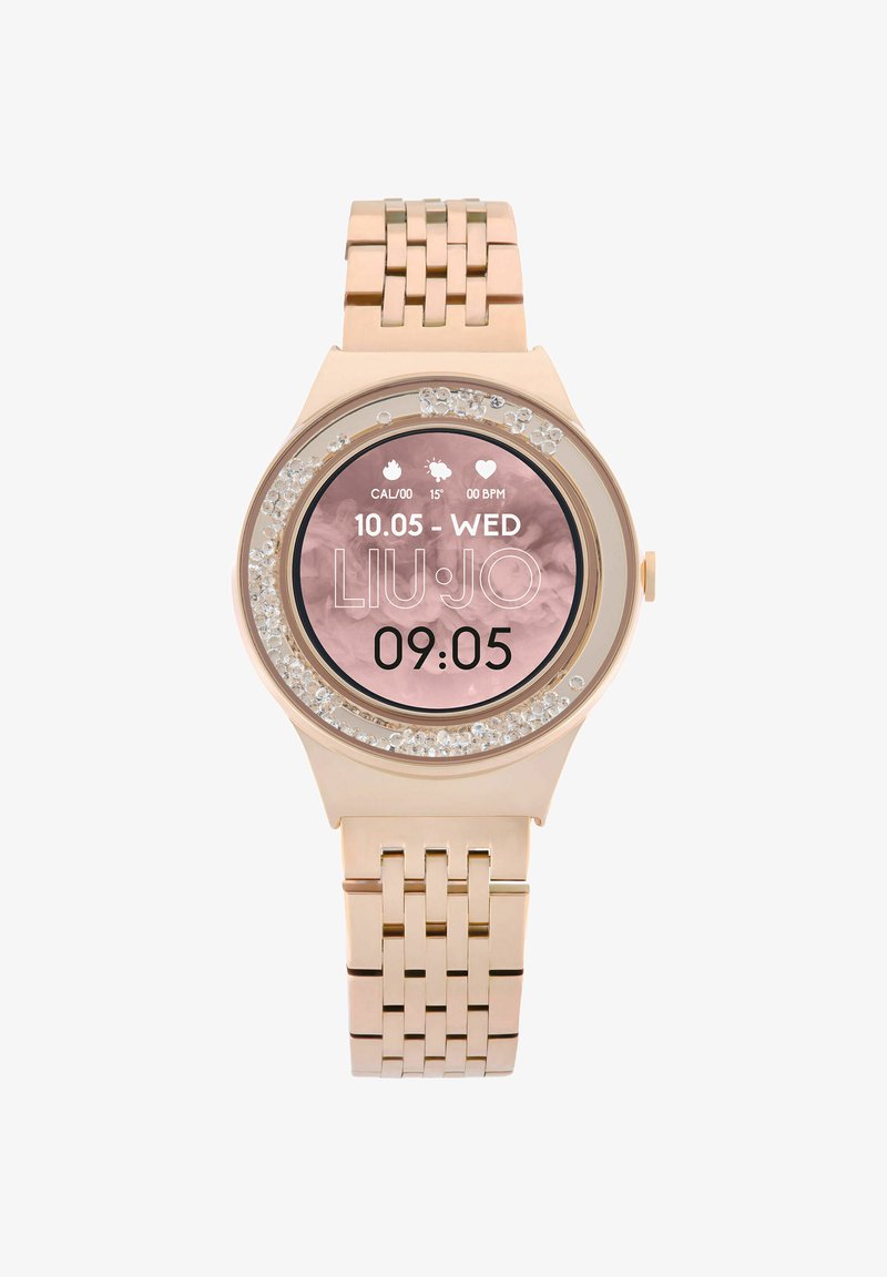 Smartwatch color oro rosa con un quadrante rotondo, accentato da cristalli attorno al display e un bracciale a maglie in metallo. Mostra ora e data.