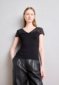 T-shirt noir avec des manches en dentelle courtes, col en V et une silhouette ajustée. Associé à un pantalon en cuir noir ample, mettant en valeur le contraste de textures.