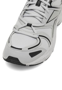 Zbliżenie na szare buty sportowe z czarnymi akcentami, siatkową cholewką, szczegółowym przeszyciem oraz cętkowaną białą i czarną podeszwą.