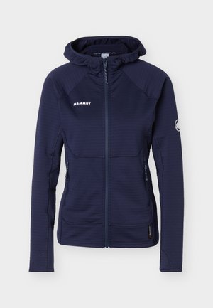 Giacca con cappuccio Mammut blu navy con chiusura frontale con cerniera, tasche laterali con zip e patch con logo sul petto e sulla manica sinistra.