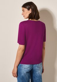 Chemise fuchsia à manches courtes avec un col rond, texture lisse et coupe décontractée, associée à un jean en denim bleu clair délavé.