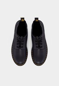 Chaussures en cuir noir avec une texture lisse, bout arrondi et coutures jaunes. Dotées d'un design à lacets et d'une boucle au talon pour un enfilage facile.