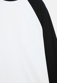 Hvid bomulds-T-shirt med sorte raglanærmer. Har en rund halsudskæring og en glat tekstur, der fremhæver farvekontrasten mellem kroppen og ærmerne.