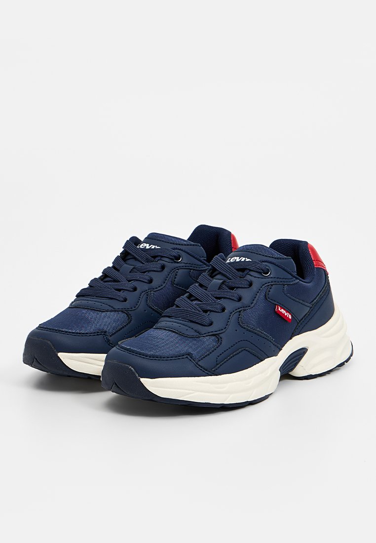 Zapatillas deportivas azul marino con un upper texturizado, suela blanca y detalles rojos. Cuentan con cordones y un logo cerca del talón. Diseño de puntera redondeada.