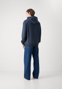 Navy hettegenser med teksturert finish og stor hette, kombinert med vide, blå jeans. Enkel, uformell design med en avslappet passform.