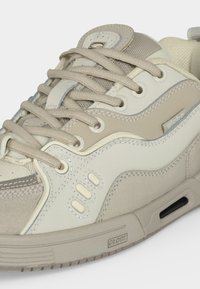 Baskets de la marque Globe beige et blanc cassé avec lacets à l'avant, languette en mesh et semelle rembourrée avec un petit détail d'aération.