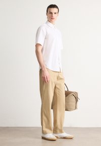 Camisa blanca de botones de manga corta, pantalones beiges, zapatillas blancas y un bolso marrón. Tela suave, ajuste relajado y detalles mínimos.