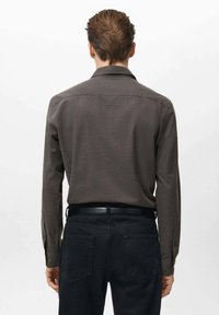 Camisa marrón de manga larga con botones y tejido texturizado, canesú trasero y pantalones negros. Cuenta con cuello y cinturón negro.