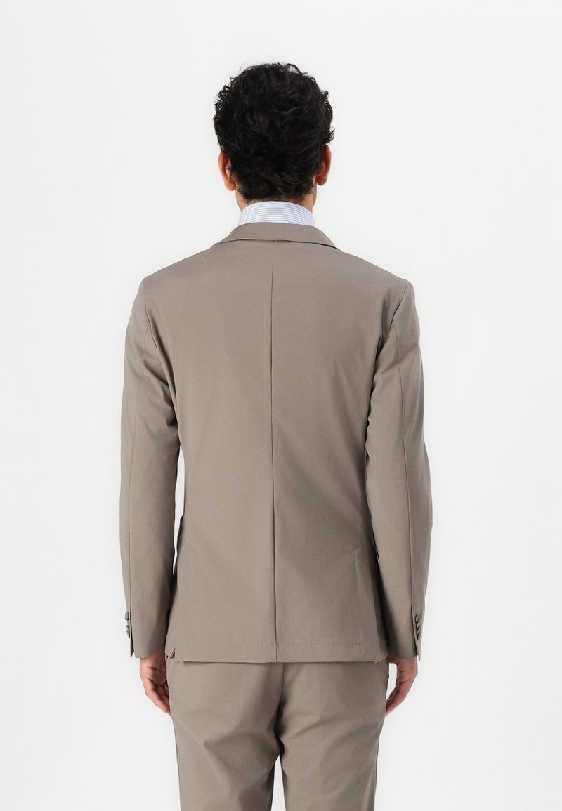 Veste de costume beige clair avec une texture lisse, un design structuré, des revers crantés et une fente simple à l'arrière. Coupe ajustée et détails minimalistes.