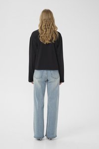 Juodas trumpintas ilgomis rankovėmis palaidinė derinama su šviesiai mėlynais plačiomis kojomis džinsais, pasižyminčiais klasikiniu penkių kišenių dizainu ir suplėšytais siūlės galais.