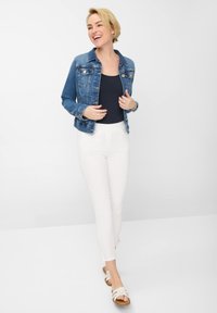 Denim jacket met voorzakken, lichtblauwe kleur, gedragen over een marineblauw top. Witte fitted broek en beige sandalen met een geweven ontwerp.