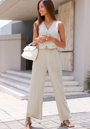 Cremefarbene, weit geschnittene Hosen kombiniert mit einer gestreiften, ärmellosen Weste. Details sind ein Knopfverschluss und eine strukturierte weiße Handtasche.