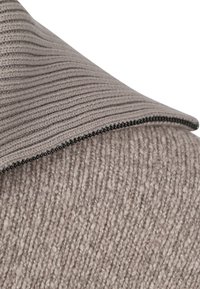 Close-up of two overlapping knitted cushions in beige and taupe with textured rib and loop patterns and a visible black zipper.