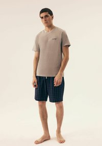 Szary t-shirt z dekoltem w serek o fakturowym wykończeniu oraz małym logo, zestawiony z granatowymi szortami z siatką w czerwoną i białą kratkę.