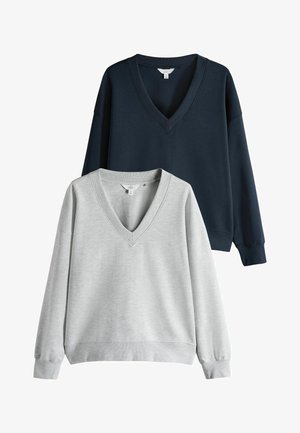 Du tirštos kaklo megztiniai sudėti vienas ant kito: vienas tamsiai mėlynas, kitas šviesiai pilkas, demonstruojantys jų laisvą siluetą ir švelnų audinį.