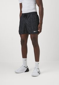 Pantaloni scurți sport negri cu un model texturat al logo-ului Nike și un swoosh alb Nike. Asortați cu pantofi sport albi și șosete.