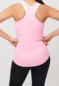 Rosa sporttopp med rundad nederkant, racerback-design och kontrasterande vita remmar. Slät textur och åtsittande silhuett.