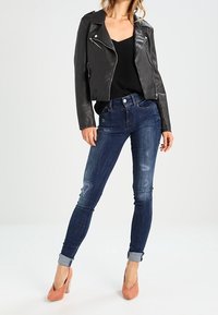 Černá kožená biker bunda, přiléhavý černý top, oprané tmavě modré skinny džíny se zahnutými nohavicemi a růžové vysoké podpatky.