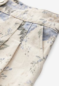 Blommönstrat tyg med blå och gröna blommor på beige bakgrund, med strukturerad bomull och synliga veck längs kanten.