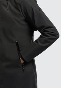 Veste noire imperméable avec une poche zippée, texture lisse, fermeture à boutons à l'avant et capuche avec cordon de serrage ajustable.