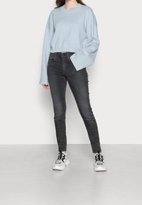 Suéter corto azul claro con mangas amplias, combinado con jeans ajustados de cintura alta en gris oscuro y zapatillas blancas gruesas.