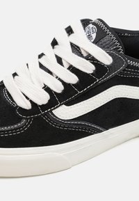 Black suede sneaker with white laces, featuring a white curved side stripe and visible stitching details. Rubber sole for grip.