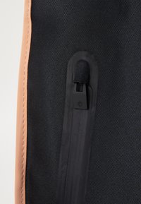 Sac en tissu noir texturé avec un accent en simili cuir beige et une fermeture éclair noire. Détails notables incluant un tirette de fermeture éclair en boucle et des coutures contrastées.