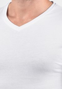 Fehér pamut V-nyakú rövid ujjú póló; sima textúra, testhez álló kialakítás és a anyagon jól látható közepes rugalmasság.