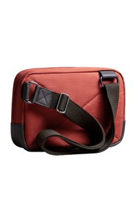 Borsa rettangolare di tessuto rosso con dettagli in pelle marrone, texture imbottita, tracolla regolabile e motivo trapuntato sulla parte frontale.