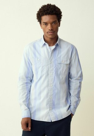 Vaaleansininen napitettava paita, jossa on pystysuorat raidat, pitkät hihat, kaksi rintataskua ja klassinen kaulustyyli. Puuvillamateriaali.