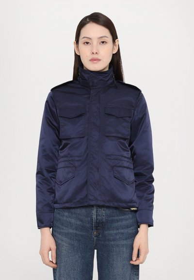 Veste en nylon bleu marine avec un col montant, deux poches poitrine et deux poches latérales, et tissu texturé. Coupée de manière courte.