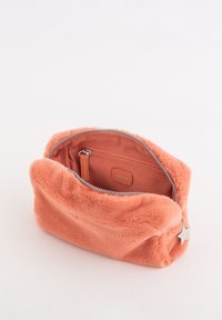 Orange fluffy stofpose med lynlåslukning, der har en glat inderforing og en lille sølvstjernevedhæng fastgjort.