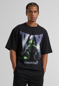 Musta puuvillapaita, jossa on graafinen kuvasto vihreästä hahmosta "X1X" ja valkoisista sanoista "Outta This World". Rentomallinen, lyhyet hihat.