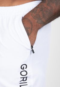 Witte shorts van een gestructureerde stof, met een ritszak en zwarte "GORILA" tekst langs de zijkant.