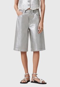 Metallic silver bermuda shorts with a loose fit, featuring side pockets and stitched hem. Paired with strappy silver sandals.