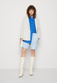 Blazer de rayas gris claro de doble botonadura sobre una camisa de botón azul, pantalones cortos azul claro, botas blancas hasta la rodilla y un pequeño bolso blanco.