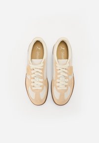 Chaussures de sport beiges avec des détails en daim et en maille. Elles présentent des lacets crème, un col rembourré et une semelle en caoutchouc. La marque "Ortholite" est visible.