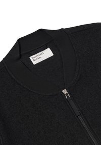 Giubbotto bomber nero caratterizzato da una texture in lana, colletto a coste e zipper frontale con hardware in metallo. L'etichetta riporta la scritta "Universal Works."