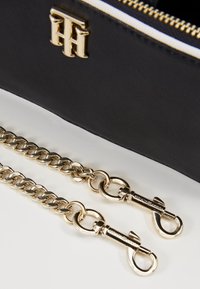 Black faux leather pouch with gold hardware and chain strap, featuring a zip closure and logo detail on the front.