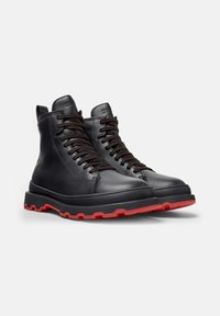 Stivali neri in pelle con lacci, suole spesse nere e treads rossi brillanti, progettati per un utilizzo intenso all'aperto.