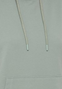 Ljusgrön hoodie-stoff med synliga dragsnören som avslutas med plastspetsar och den övre kanten av en framficka med söm.