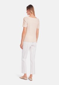 Light beige short-sleeve top with a wide neckline, paired with white pants featuring a subtle leaf pattern, and beige slip-on shoes.