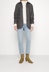 Szara koszula w kratkę z dwoma przednimi kieszeniami, noszona na kremowym swetrze. Jasnoniebieskie dżinsy i oliwkowe botki za kostkę z niskim obcasem.